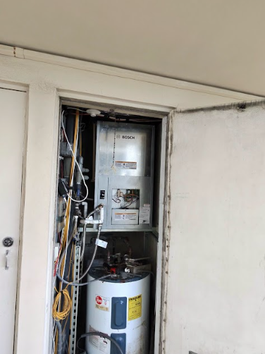 A water heater unit is enclosed in a utility closet with pipes and electrical wiring.