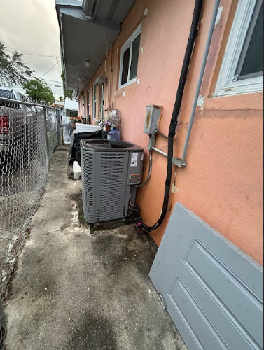 Exterior view of an air conditioner unit next to a building with a fence and a gray door.