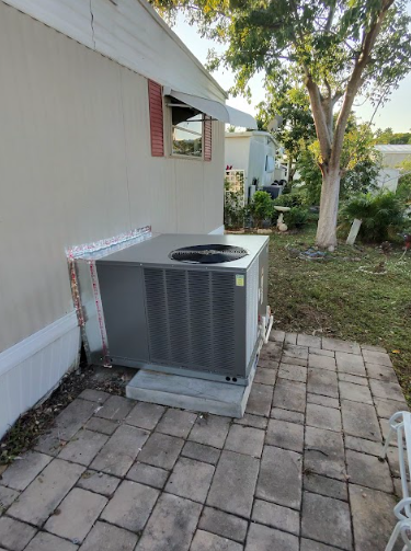 An air conditioning unit on a concrete pad outside a tan building, brick patio in foreground.