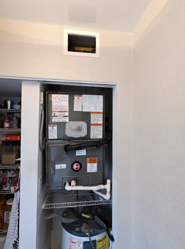 HVAC unit in a closet with a water heater. An air vent is above. White walls and a sliding door.