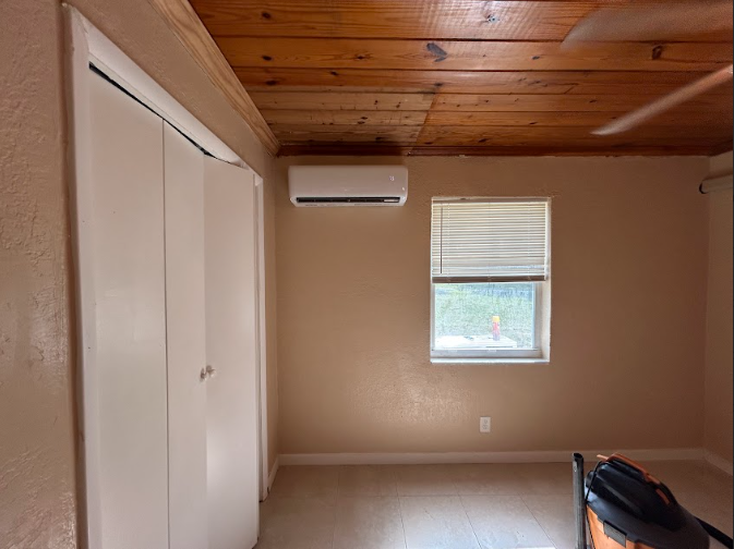 A bedroom with white closet doors, a window, and a wall-mounted air conditioning unit.