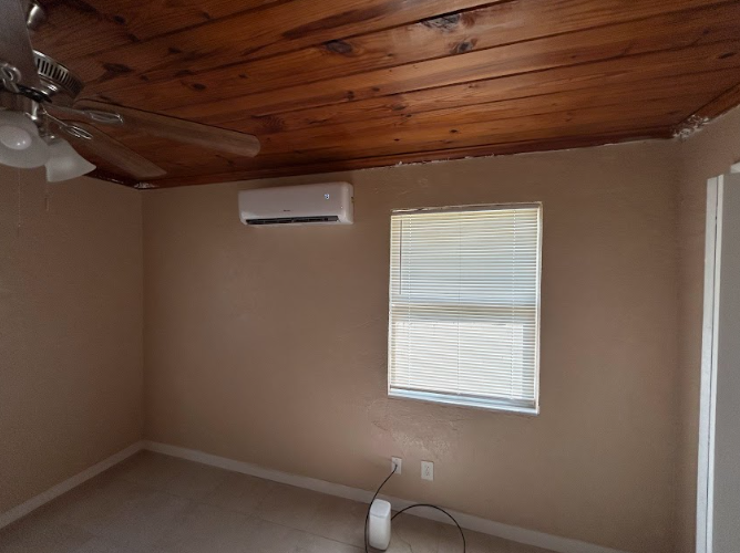 Bedroom with a wooden ceiling, beige walls, air conditioner, and a window with blinds.