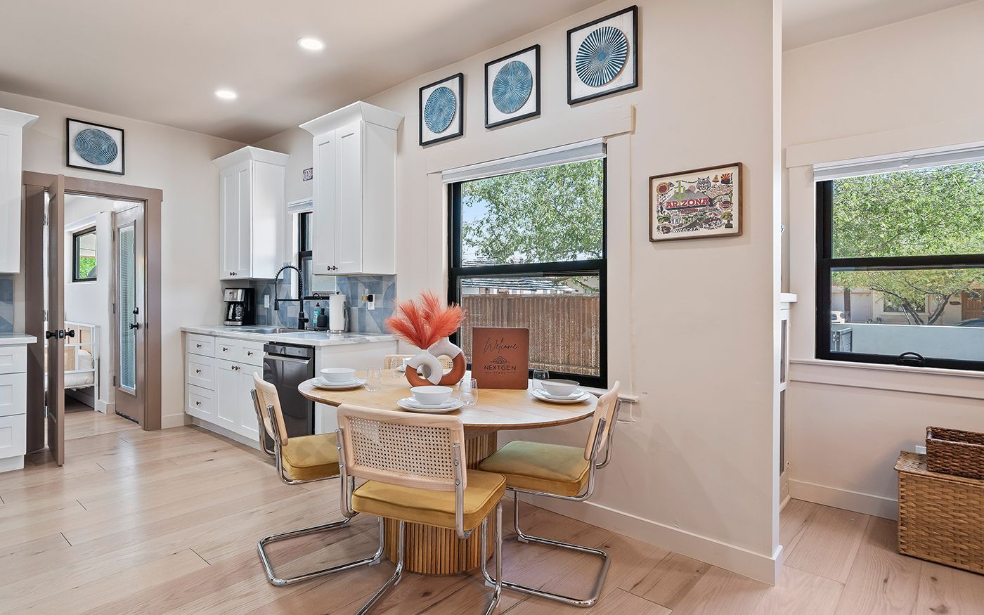 Light-filled kitchen and dining area with round table, modern chairs, and white cabinets.