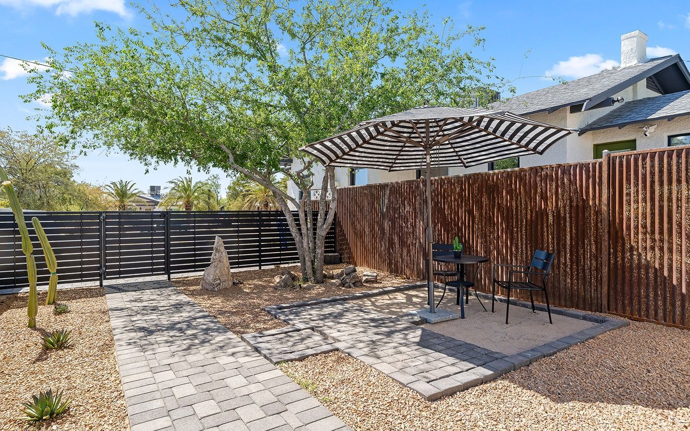 Backyard patio with seating, shade, and decorative fence, with a tree in a desert landscape.