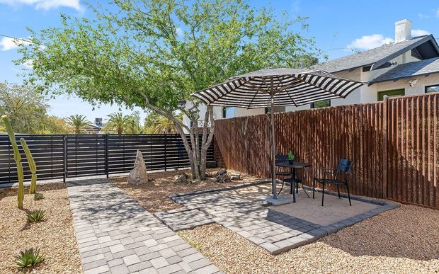 Backyard patio with seating under striped umbrella and wooden fence.