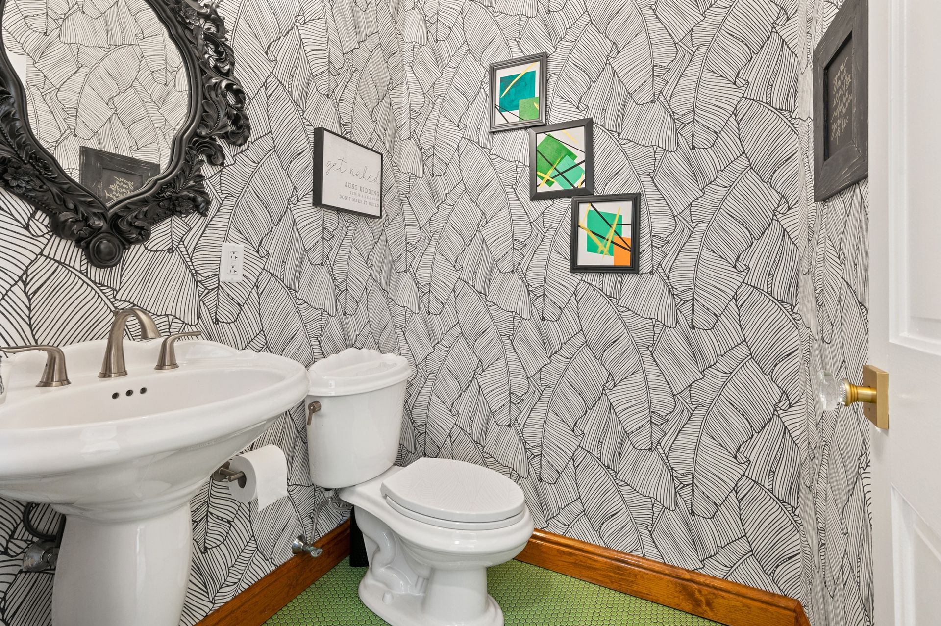 Powder room with black and white patterned wallpaper, pedestal sink, and framed artwork.