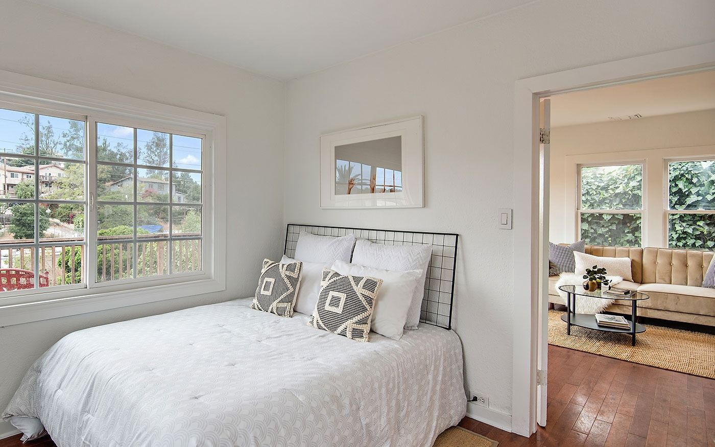 Cozy bedroom with bed, window overlooking greenery, and doorway to living area with sofa.