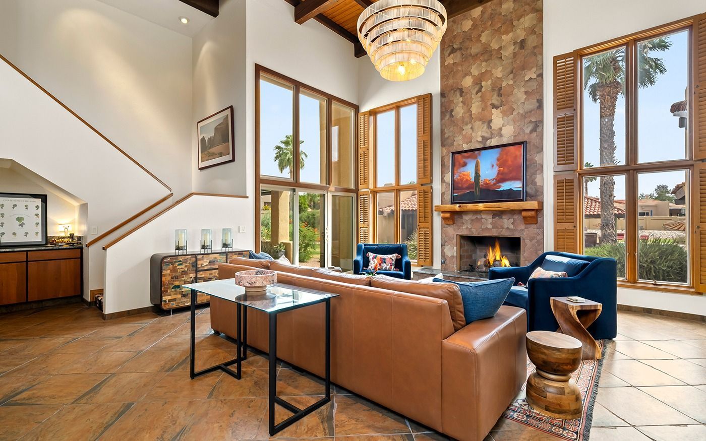 Spacious living room with high ceilings, fireplace, leather sofa, and large windows overlooking a yard.