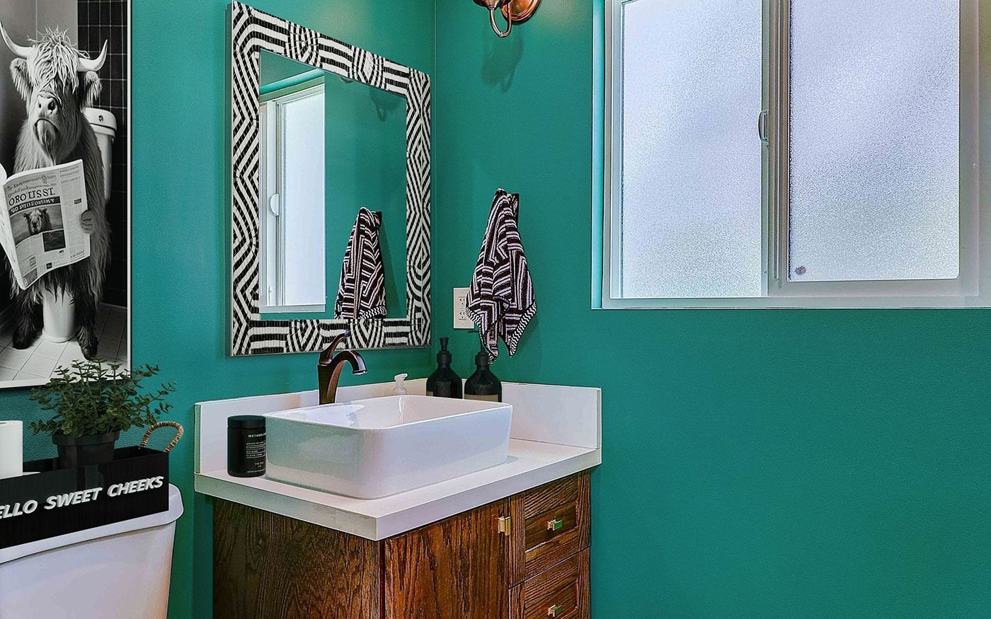 Teal bathroom with zebra-striped mirror, modern sink, and wood cabinet.