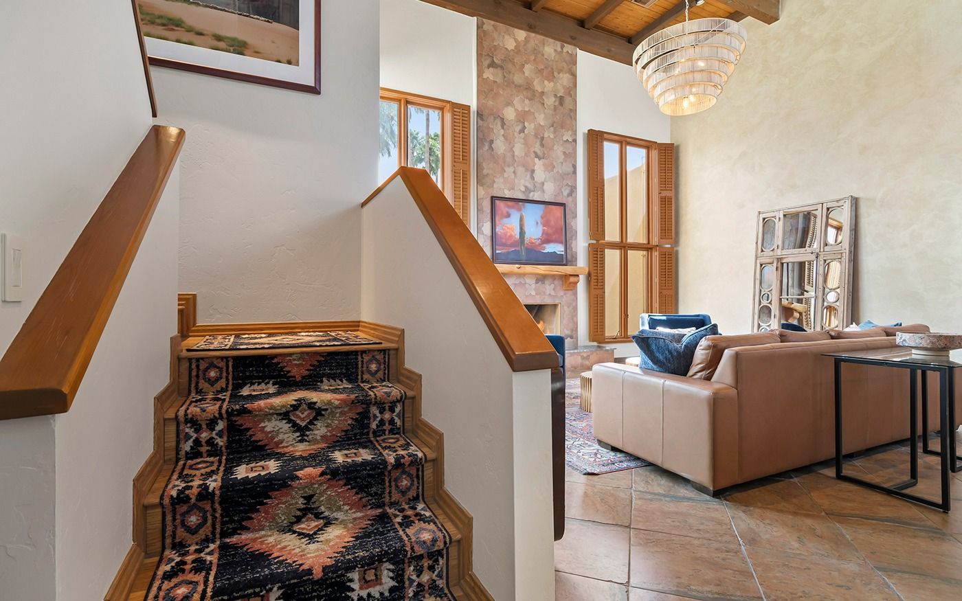 Staircase with patterned carpet leading up to a living room with a sofa, fireplace, and chandelier.