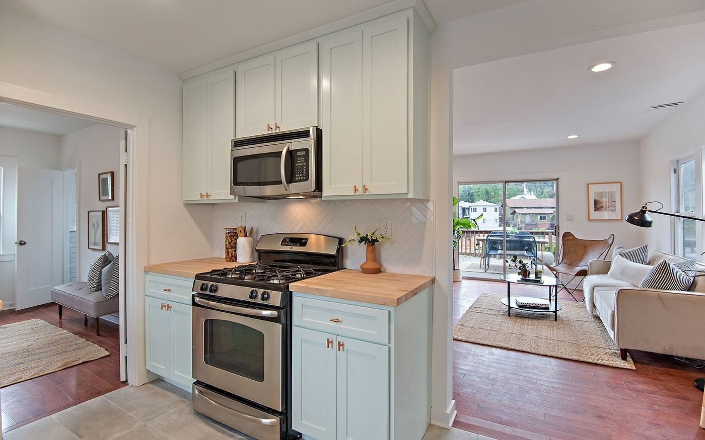Kitchen with light blue cabinets, stainless steel appliances, and wood countertops. Open to living area.