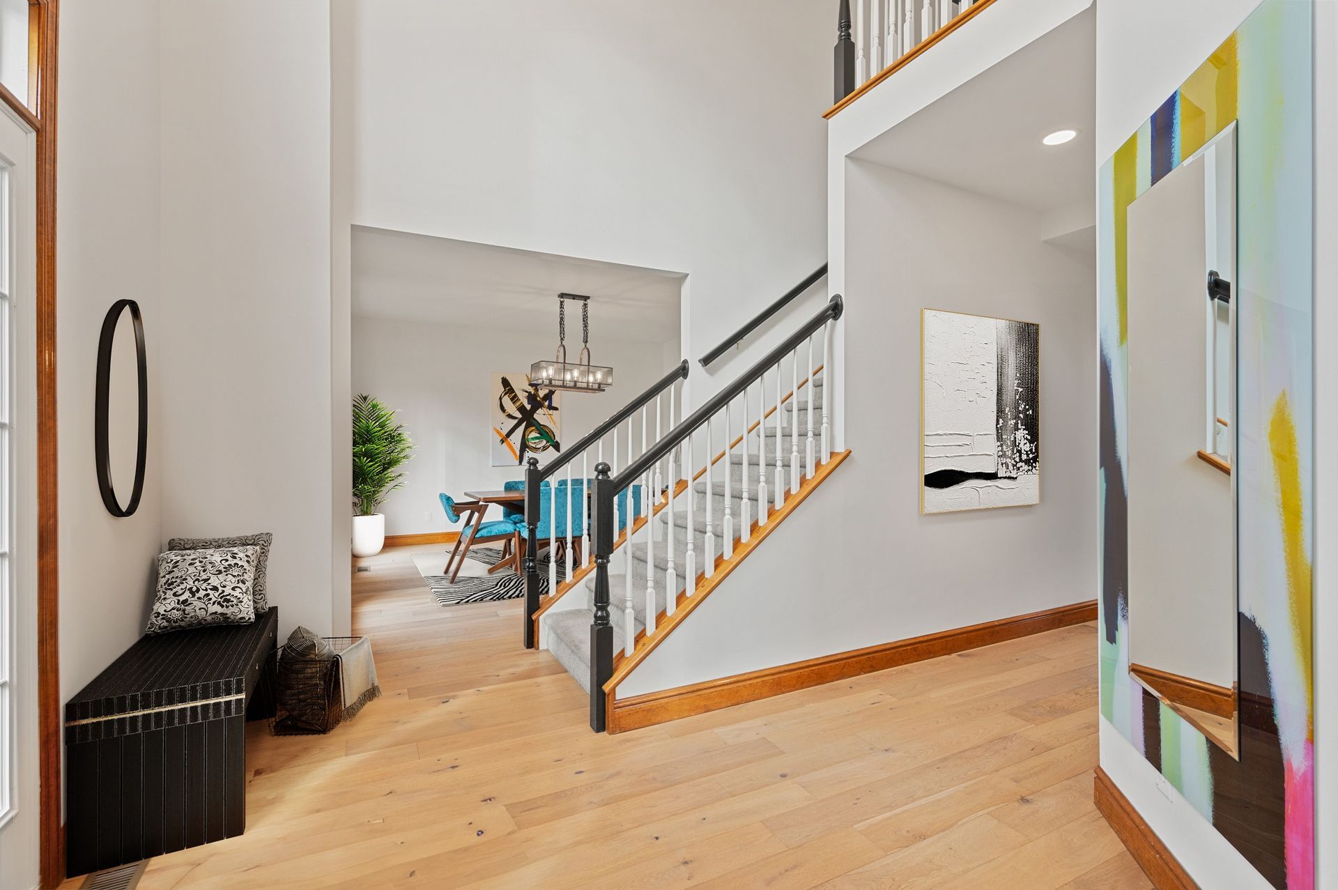 Entryway with staircase, bench, and colorful mirror. Dining room visible in the background.