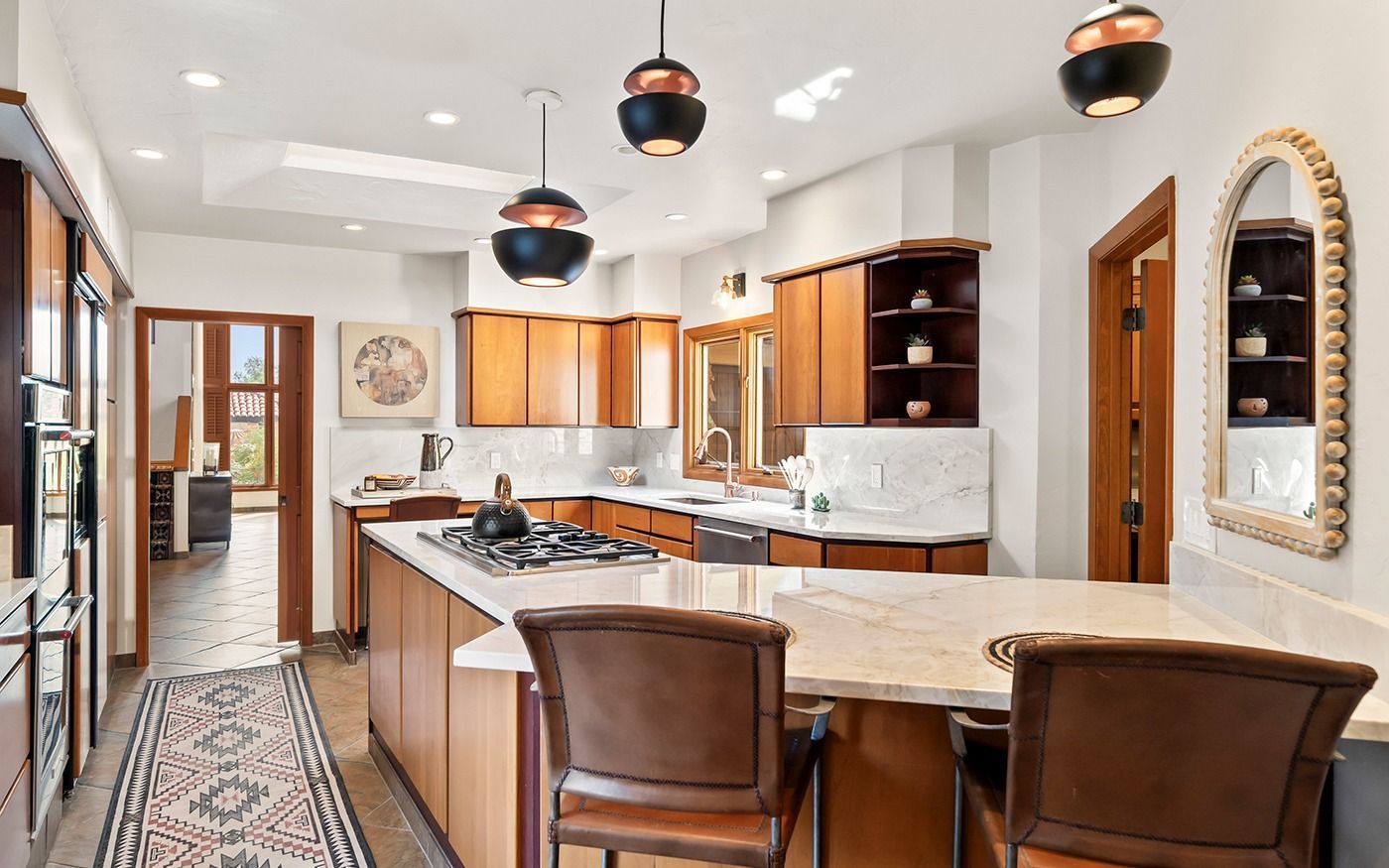 Spacious kitchen with wooden cabinetry, island, and pendant lights; two bar stools.