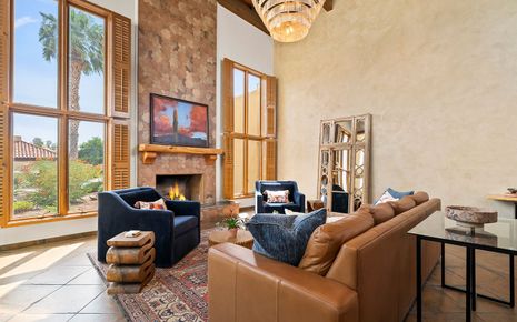 Living room with fireplace, tan leather sofa, blue chairs, and large windows.