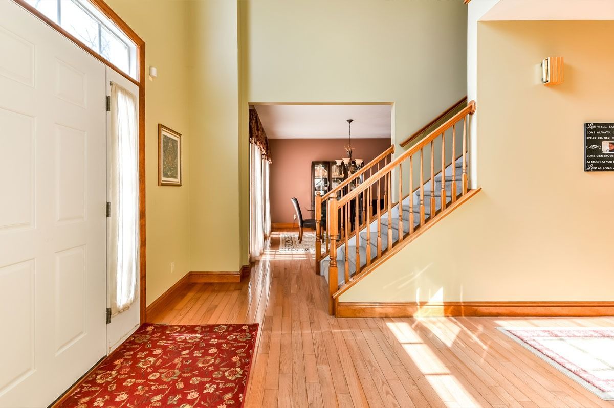 Entryway with wood floors, staircase, and red rug, leading to a dining area.