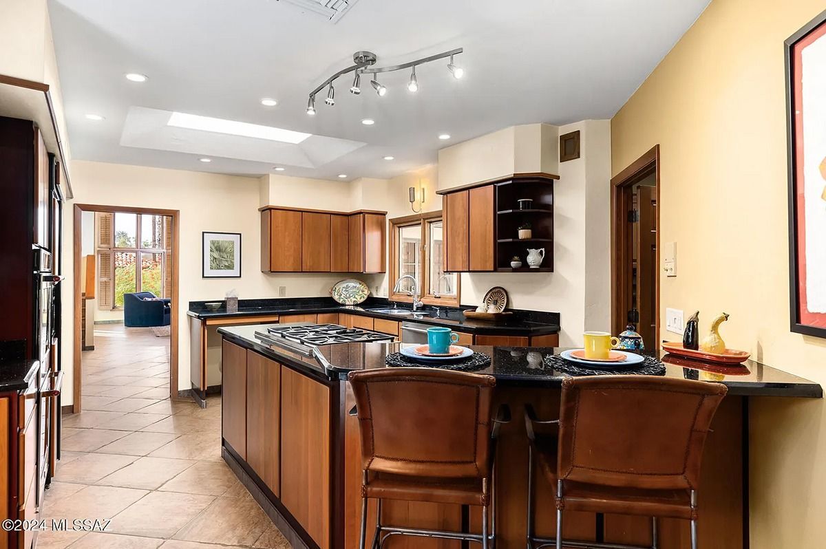 Kitchen with wooden cabinets, island, black countertops, and bar stools.