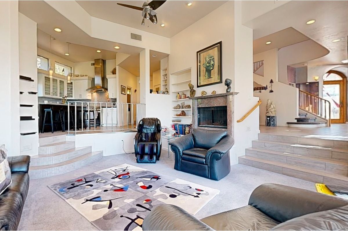 Open-concept living area with kitchen, steps, furniture, abstract rug, fireplace, and arched doorway.