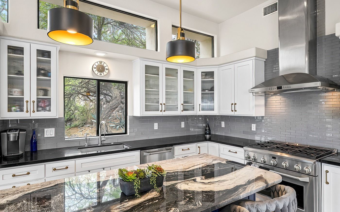 Modern white kitchen with dark countertops, stainless steel appliances, and large windows.