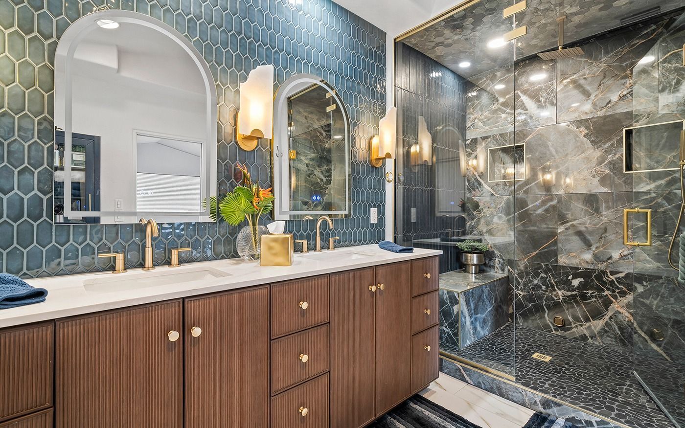 Luxurious bathroom with blue tile, wood vanity, marble shower, and arched mirrors.