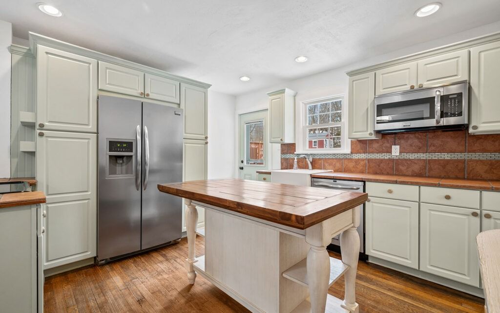 Kitchen with green cabinets, stainless steel appliances, and a wooden island on a hardwood floor.