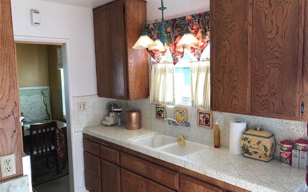 Kitchen with dark wood cabinets, white countertops, and a sink by a window with patterned curtains.