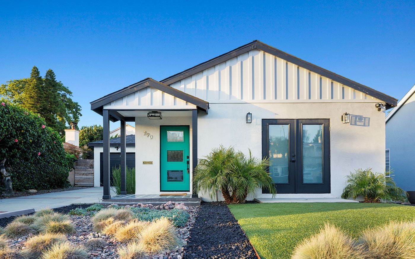 Modern white house with turquoise door, black accents, and manicured lawn.
