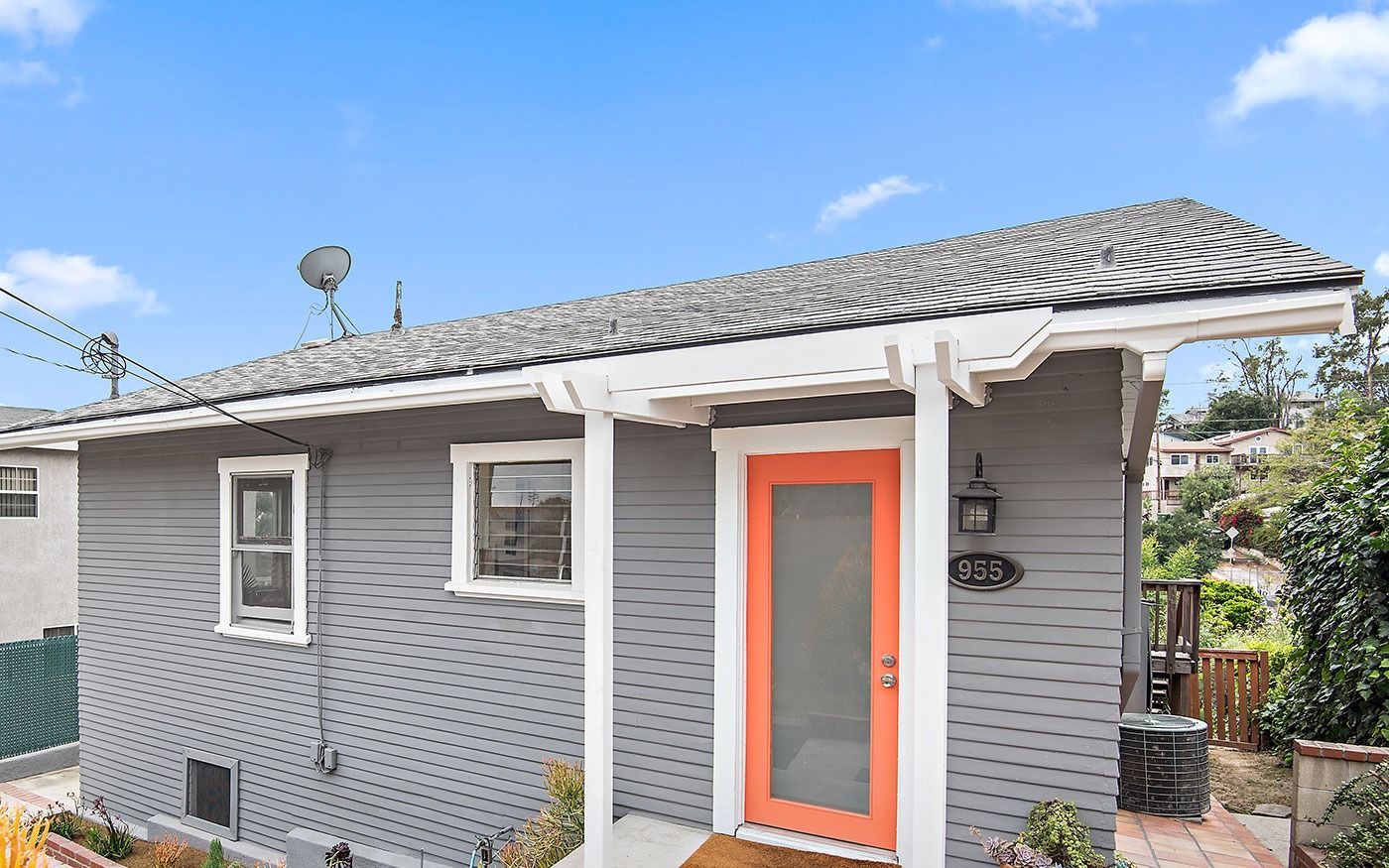 Gray house with orange door and white trim under a blue sky.