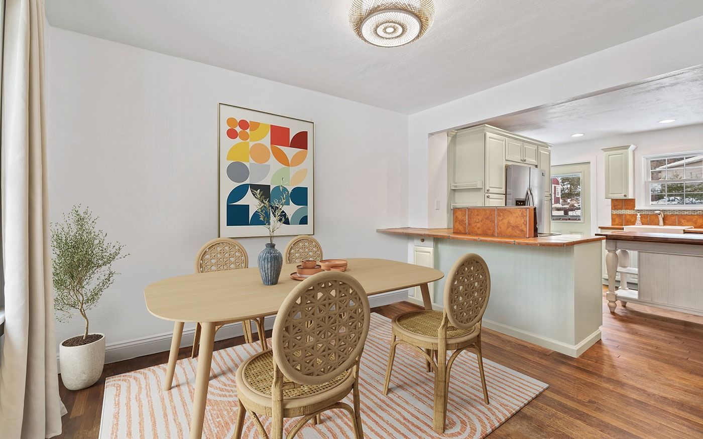 Dining room with oval table, wicker chairs, and colorful artwork. Open to a kitchen.