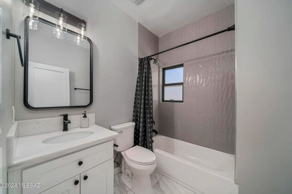 Modern bathroom with white vanity, toilet, and tub, gray walls, and black accents.