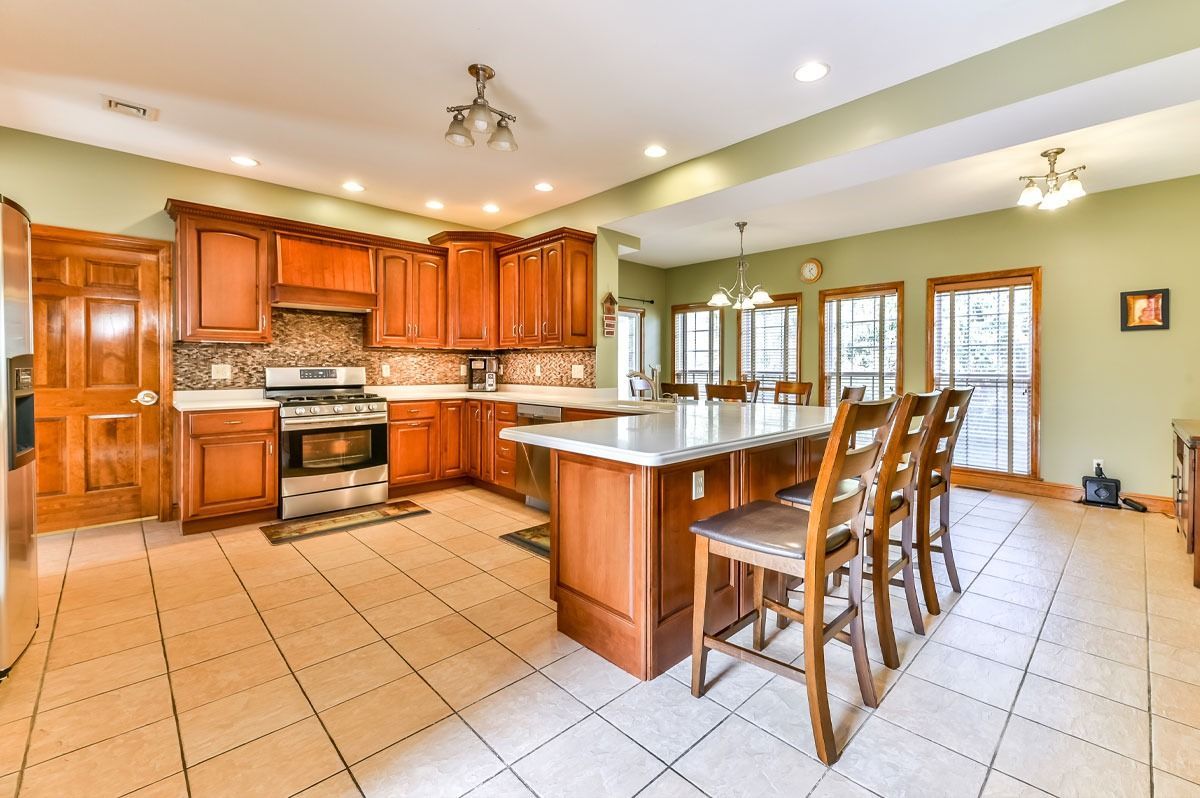 Spacious kitchen with brown cabinets, island with stools, tiled floor, and green walls.