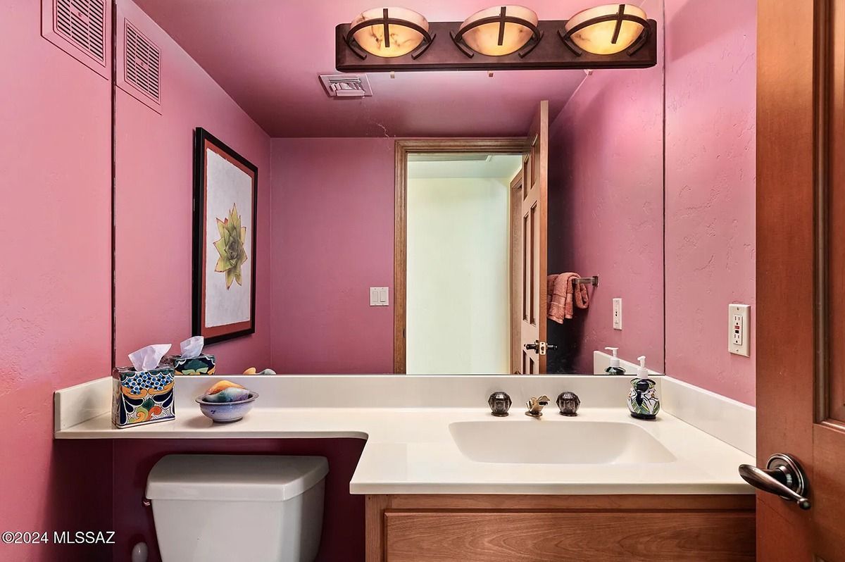 Pink bathroom with a vanity, mirror, toilet, and a partially open door.
