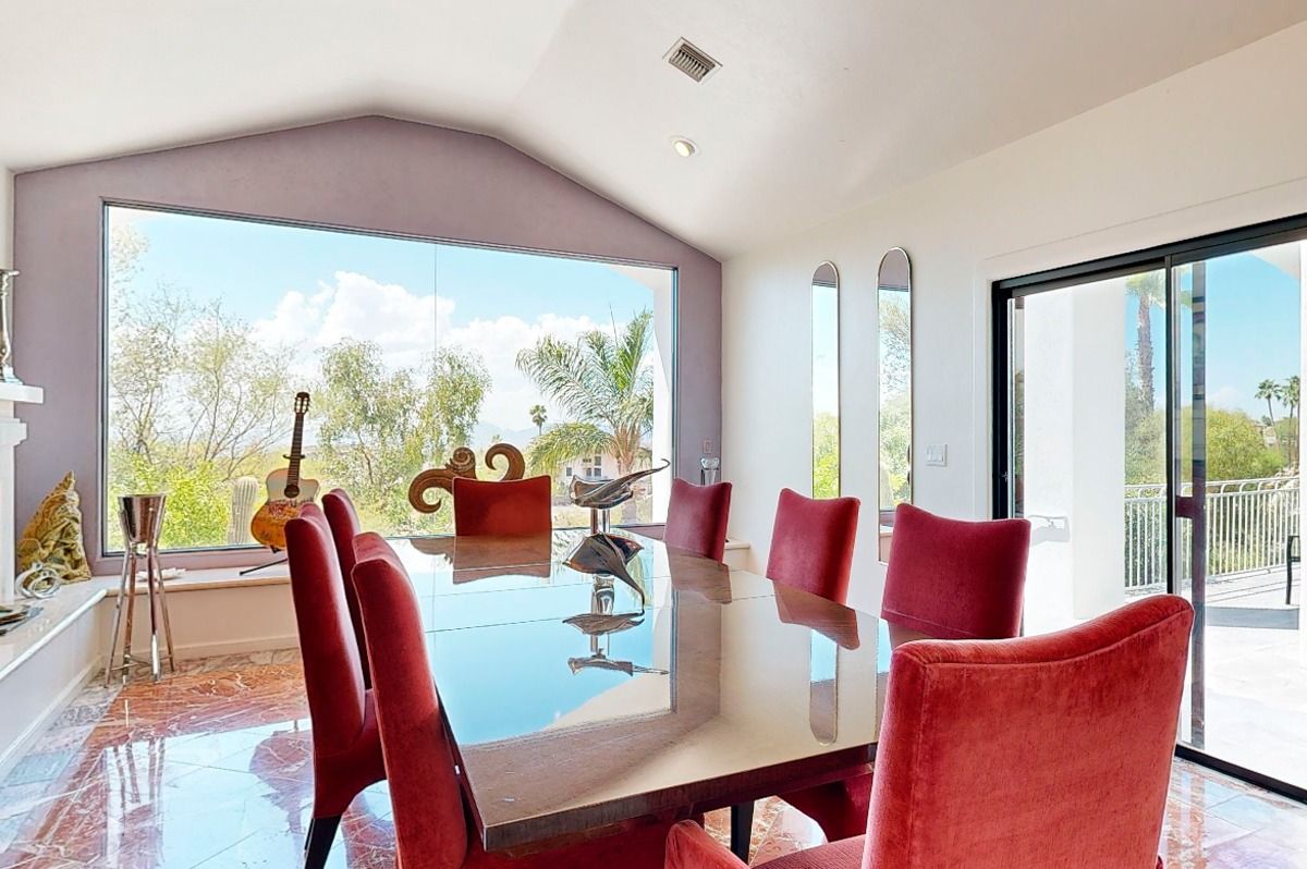 Dining room with red chairs around a reflective table, large window overlooking a mountain, and tile floor.