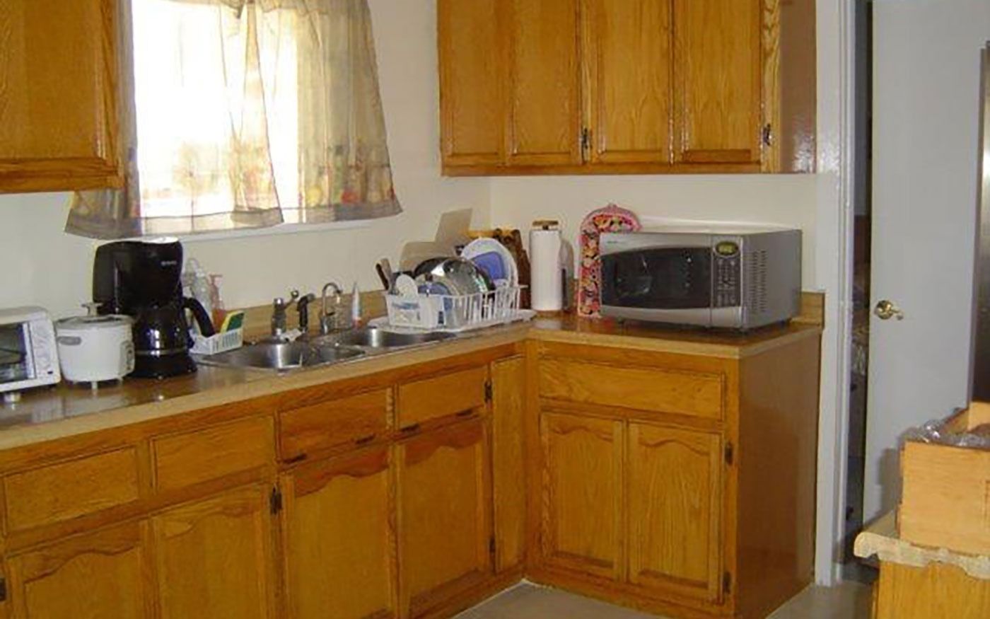 A small kitchen with wooden cabinets, a sink, microwave, and window.