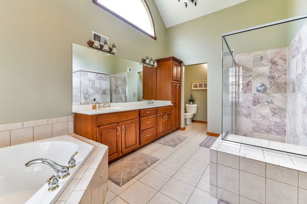 Spacious bathroom with tub, shower, and vanity; tan walls, light tile floor, wooden cabinets.