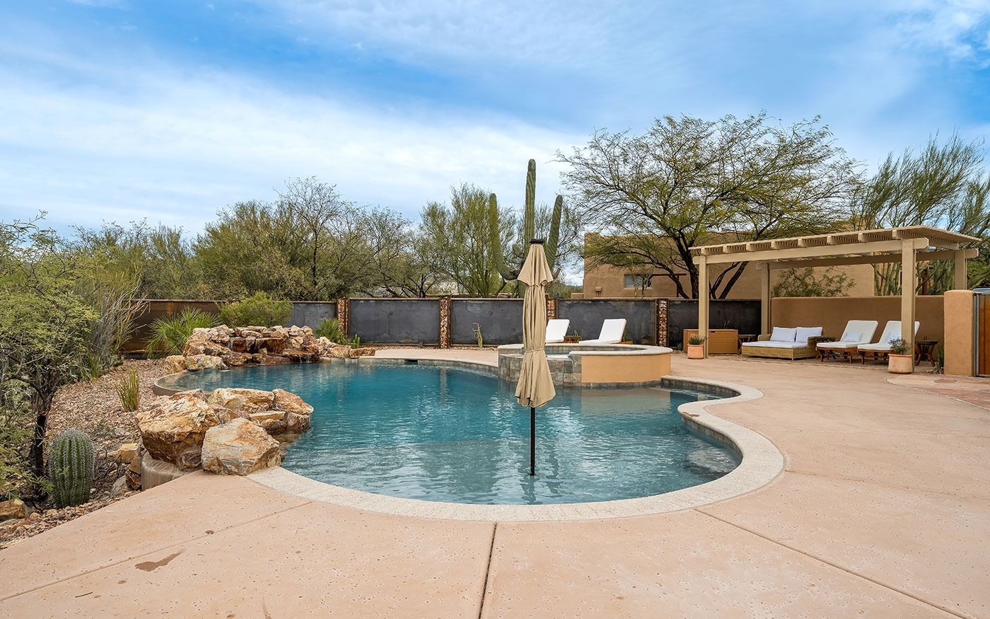 Backyard pool with lounge chairs, pergola, and desert landscaping under a blue sky.