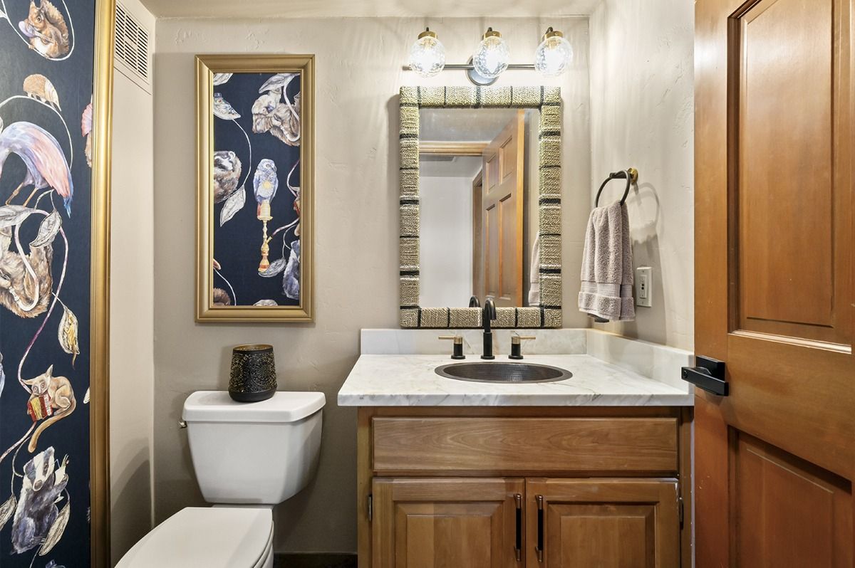Bathroom with floral wallpaper, framed art, vanity, mirror, and wooden door.