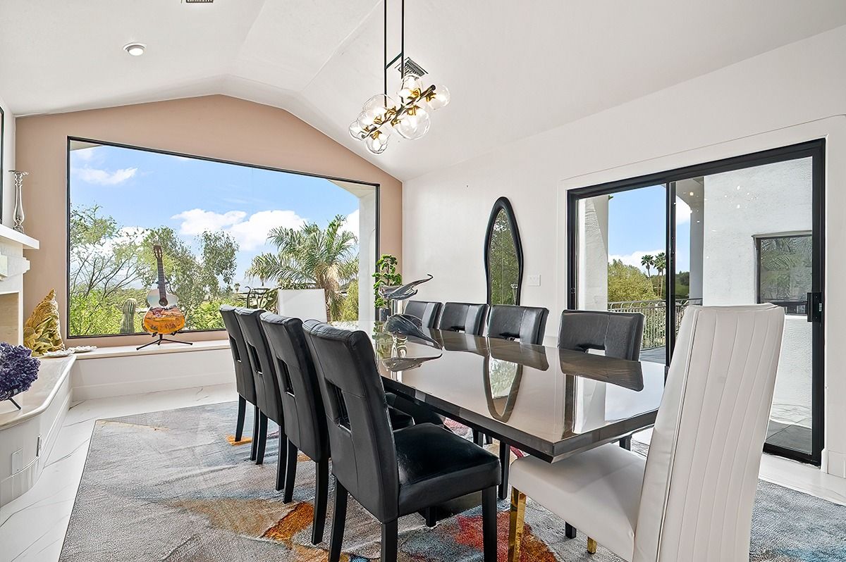 Elegant dining room with large windows, long table, modern chairs, and a view of greenery.