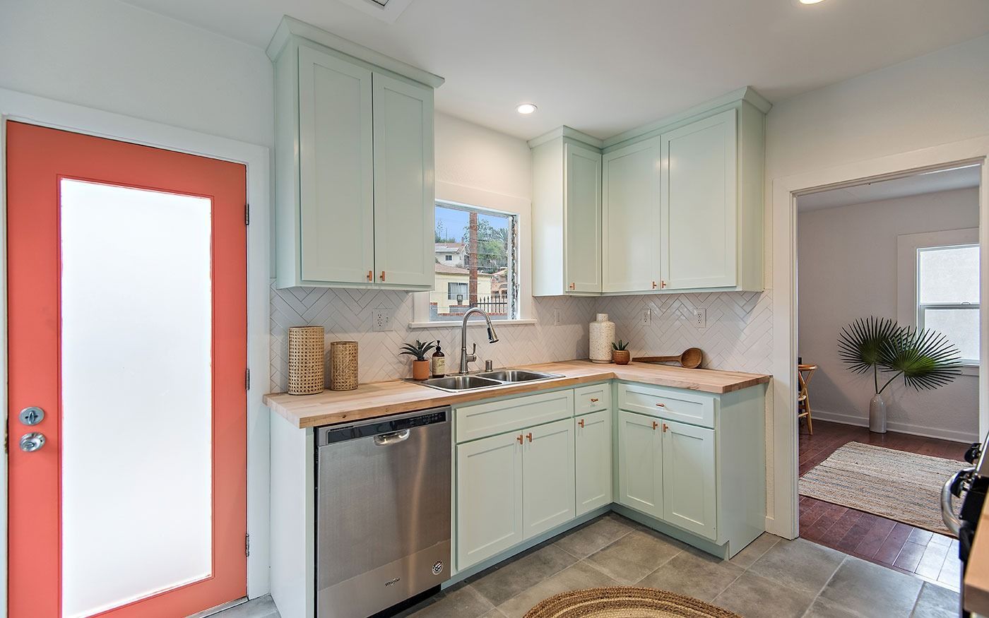 Small kitchen with light green cabinets, a stainless steel dishwasher, and a coral-colored door.