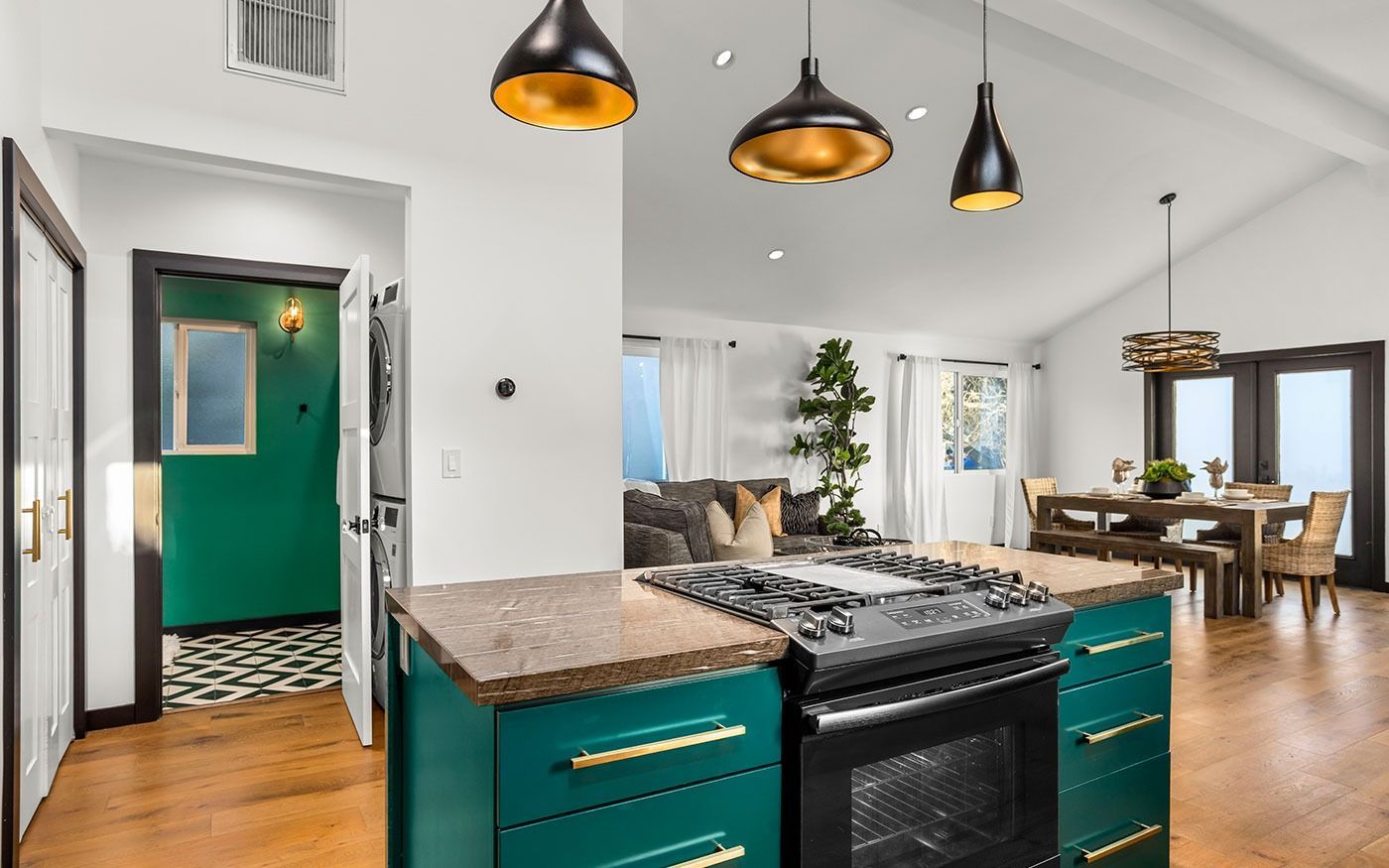 Kitchen with teal island, gold pendant lights, open to living/dining area.