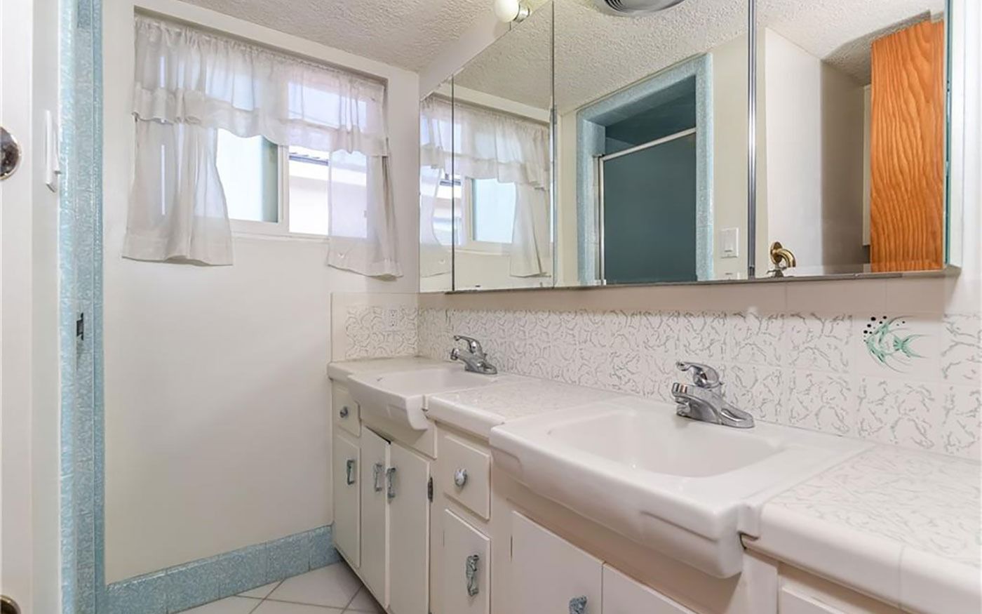 Bathroom with white sinks, cabinets, and a mosaic tile backsplash.