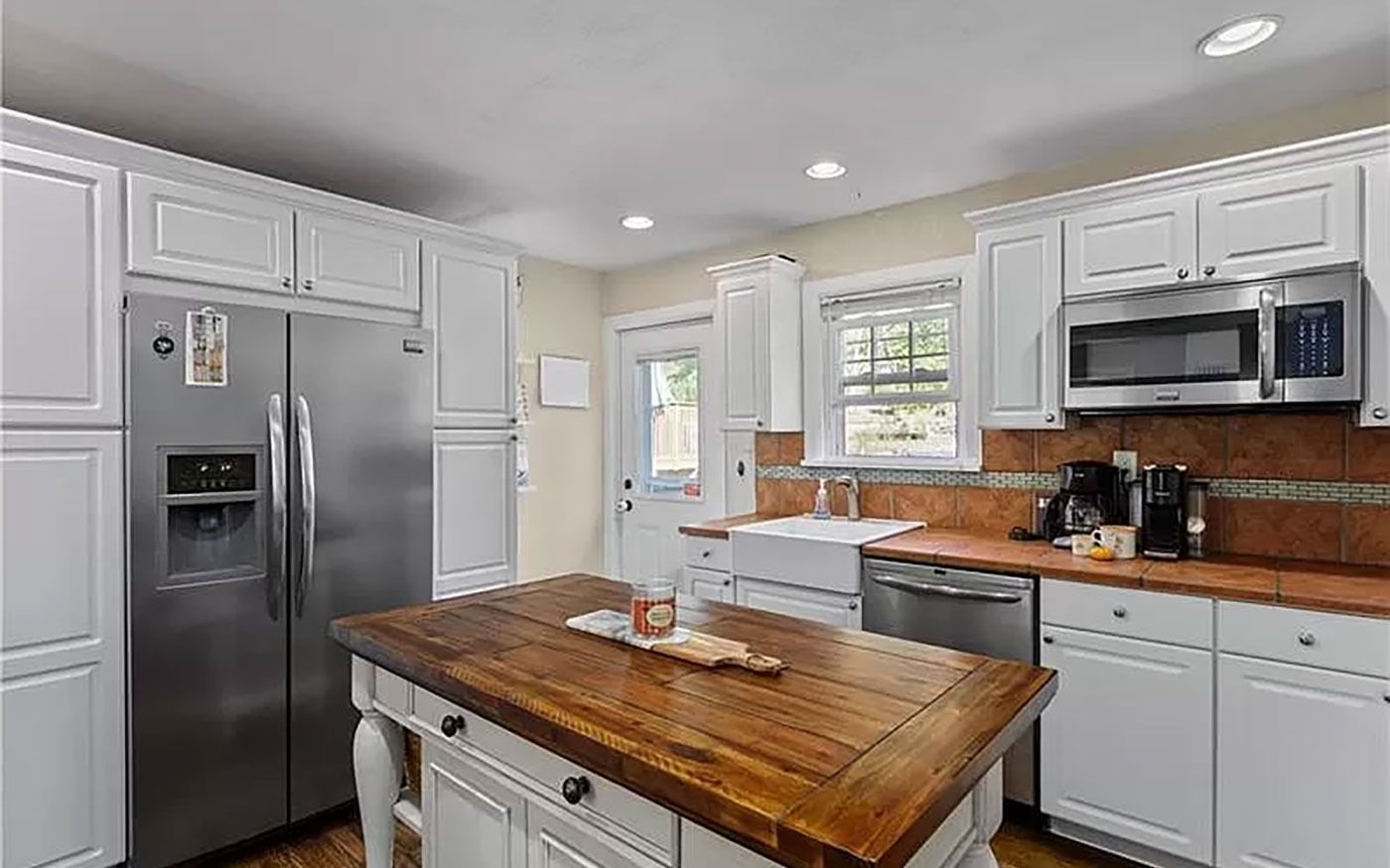 White kitchen with wood island, stainless steel appliances, and a door to the outside.