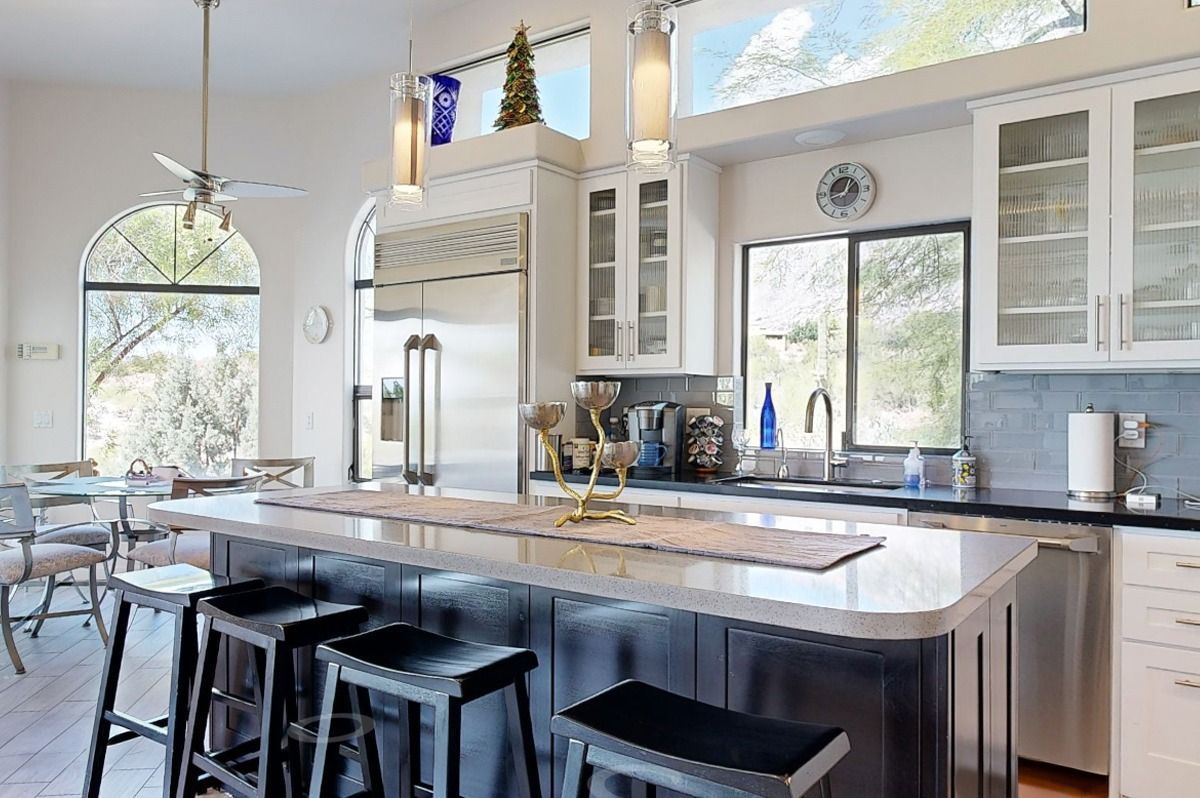 Kitchen with island, stainless steel appliances, white cabinets, arched window, and bar stools.