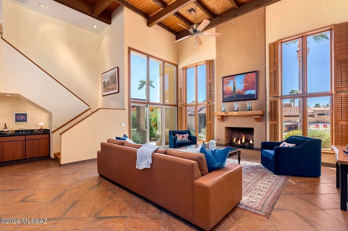 Spacious living room with high ceilings, fireplace, large windows, and brown leather sofa.