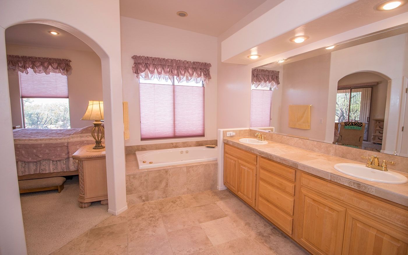 Spacious bathroom with a jacuzzi tub, double vanity, and an arched doorway to a bedroom.