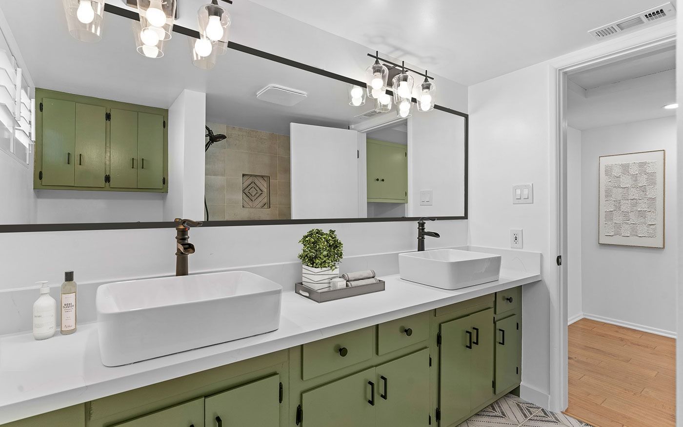 Bathroom with white countertops, two sinks, green cabinets, and a large mirror.