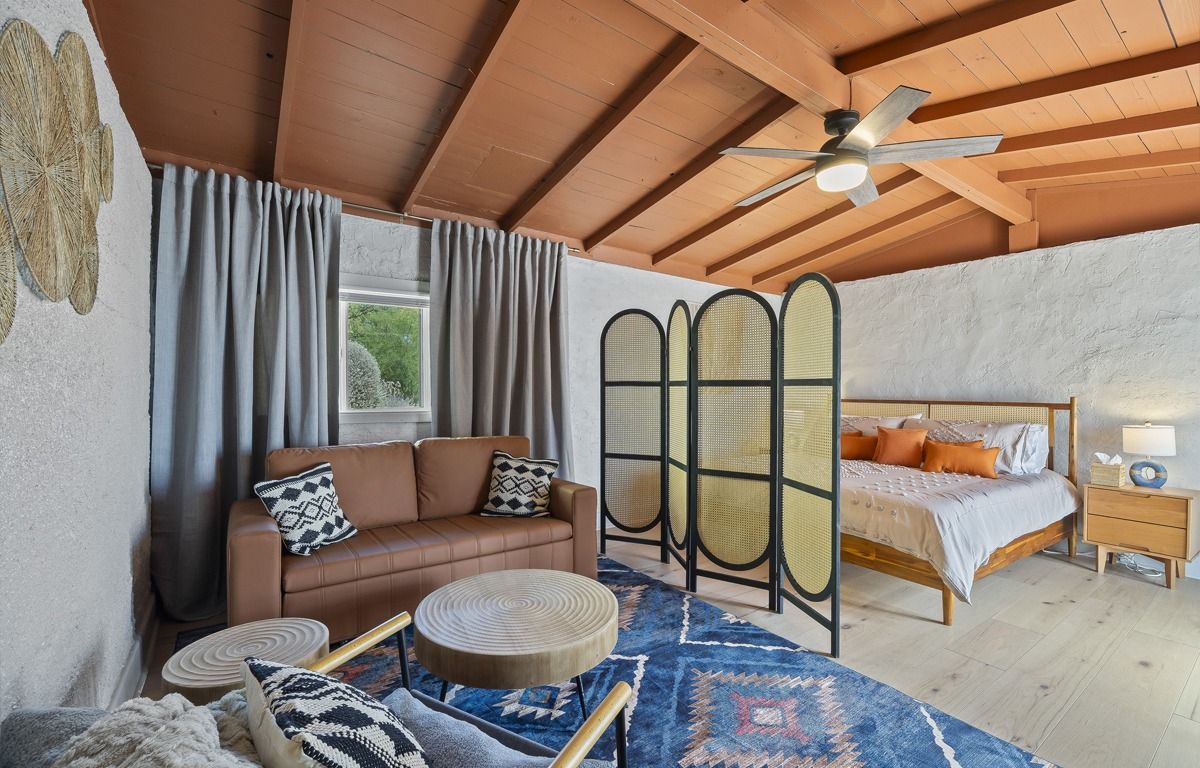 Bedroom with brown sofa, bed, room divider, blue rug, and white textured walls.
