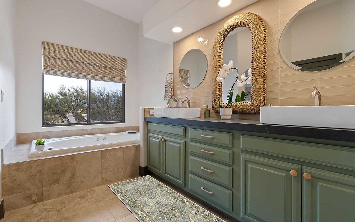 Bathroom with green cabinets, stone tub, large mirrors, and a window with a view.