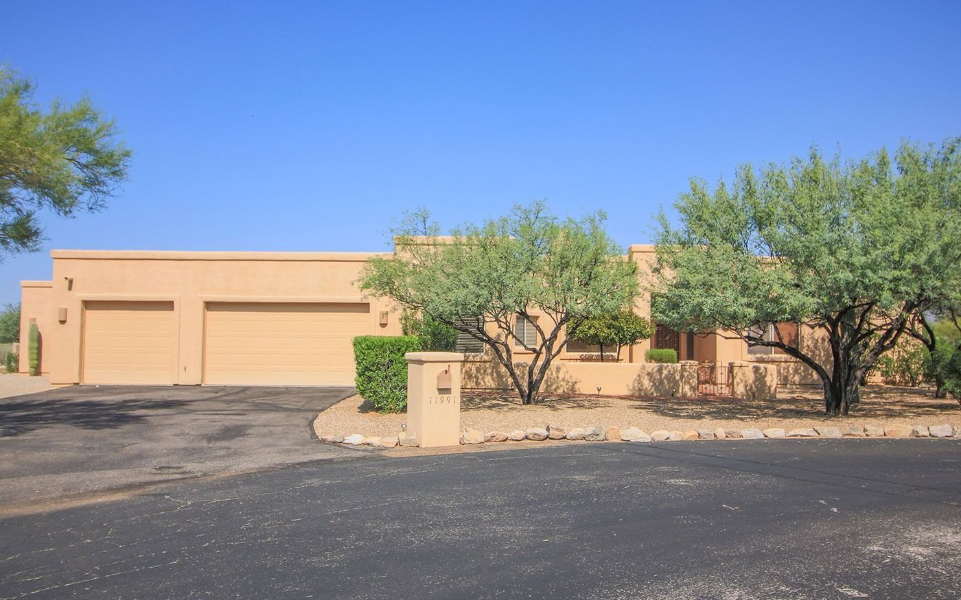 Tan stucco house with a two-car garage and desert landscaping under a blue sky.