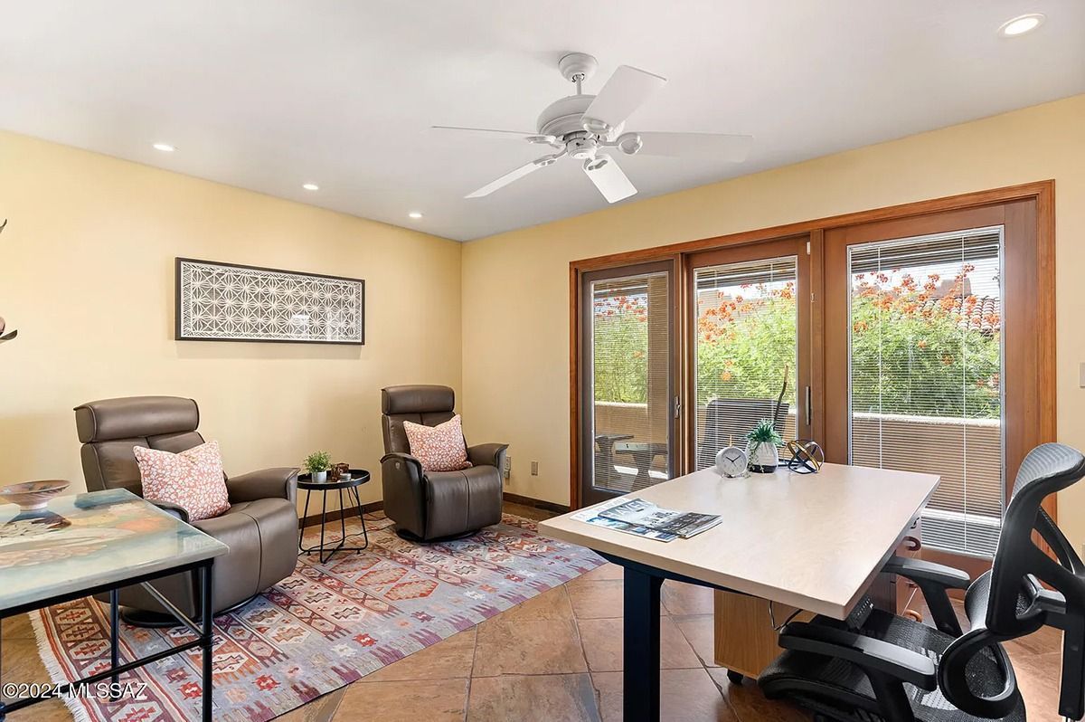 A well-lit home office with a desk, two recliners, and sliding glass doors leading to an outdoor view.