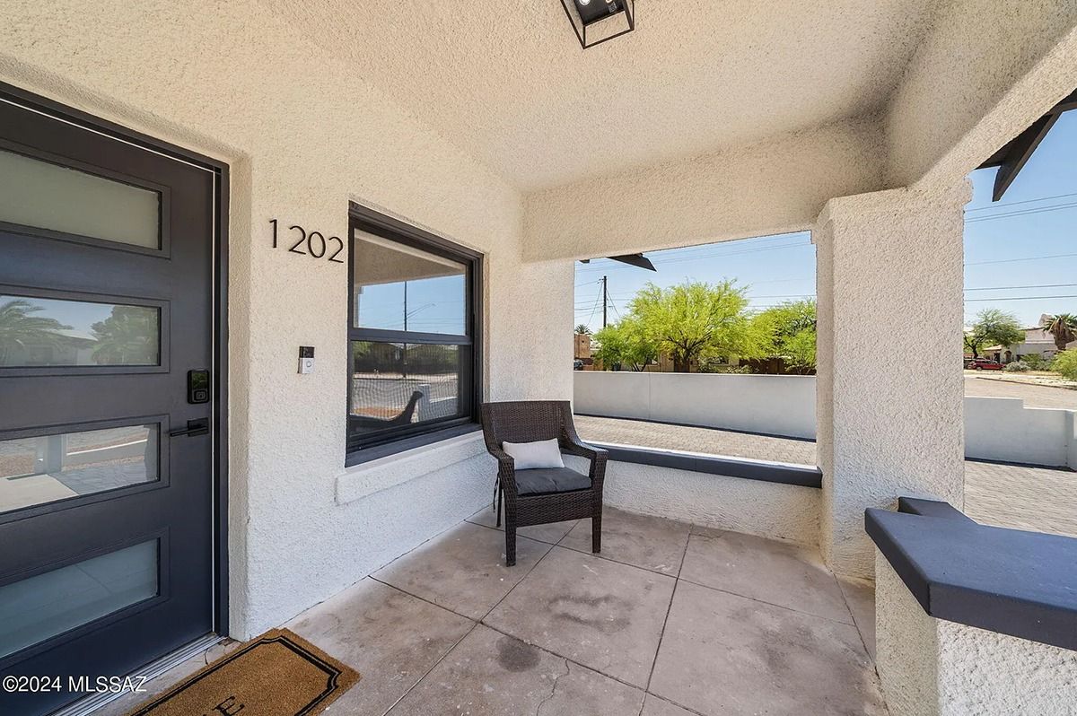 Front porch of a house with a gray door, chair, and window. House number 1202 above the door.